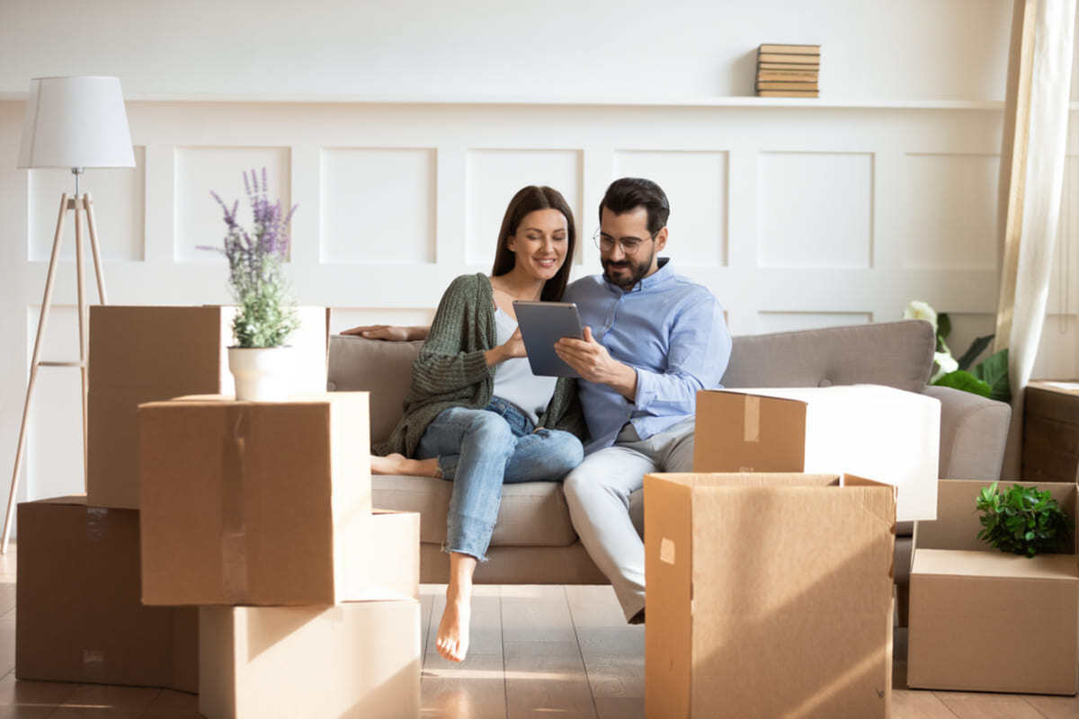 Happy couple sitting on a couch surrounded by moving boxes