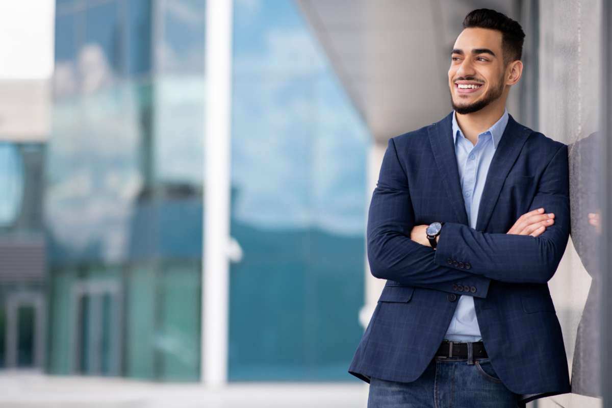 Happy millennial bearded arab man in suit wealthy businessman or CEO standing next to modern business center