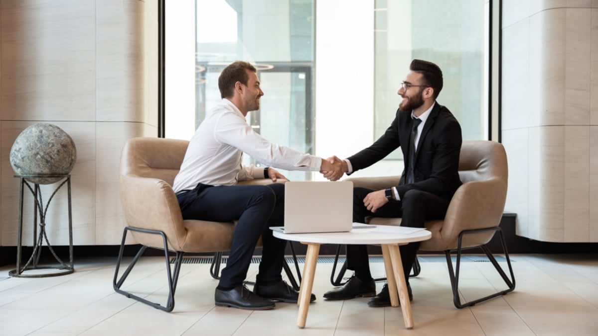 Professionals shaking hands in front of a laptop