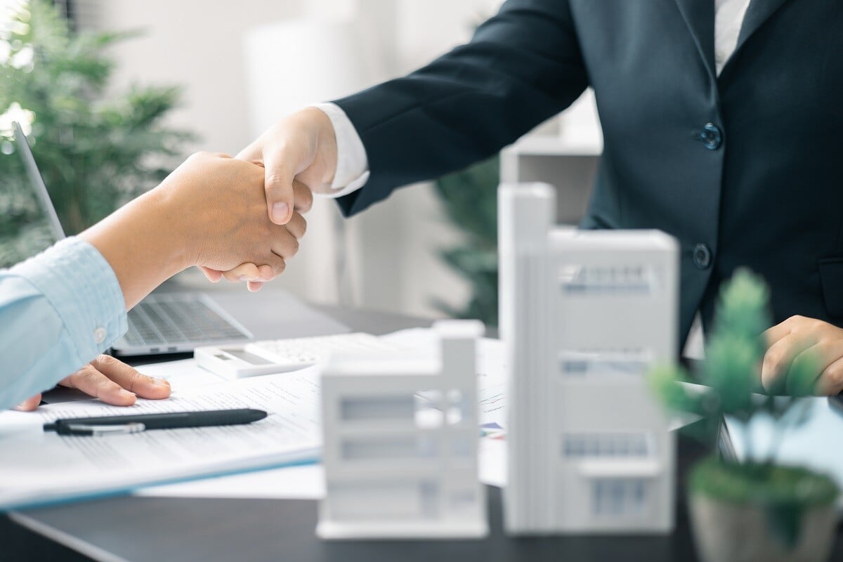 Two professionals shaking hands next to commercial property model