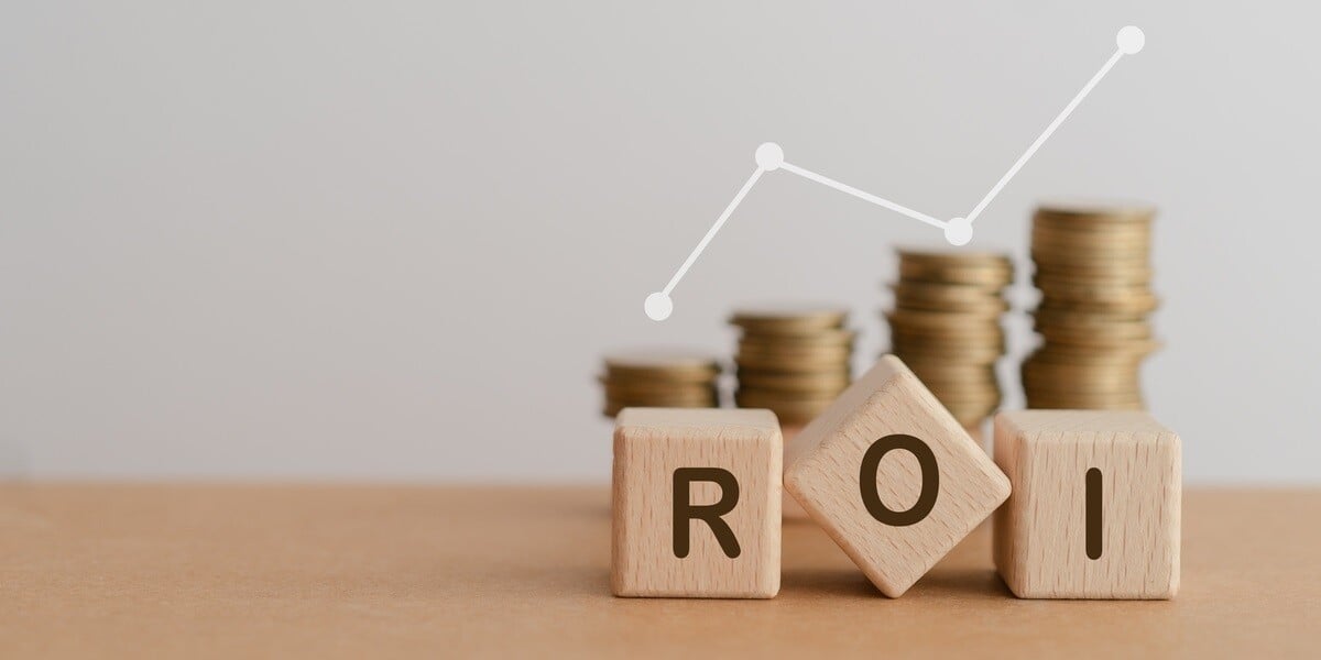 Wooden blocks spelling out ROI sitting in front of stacks of coins